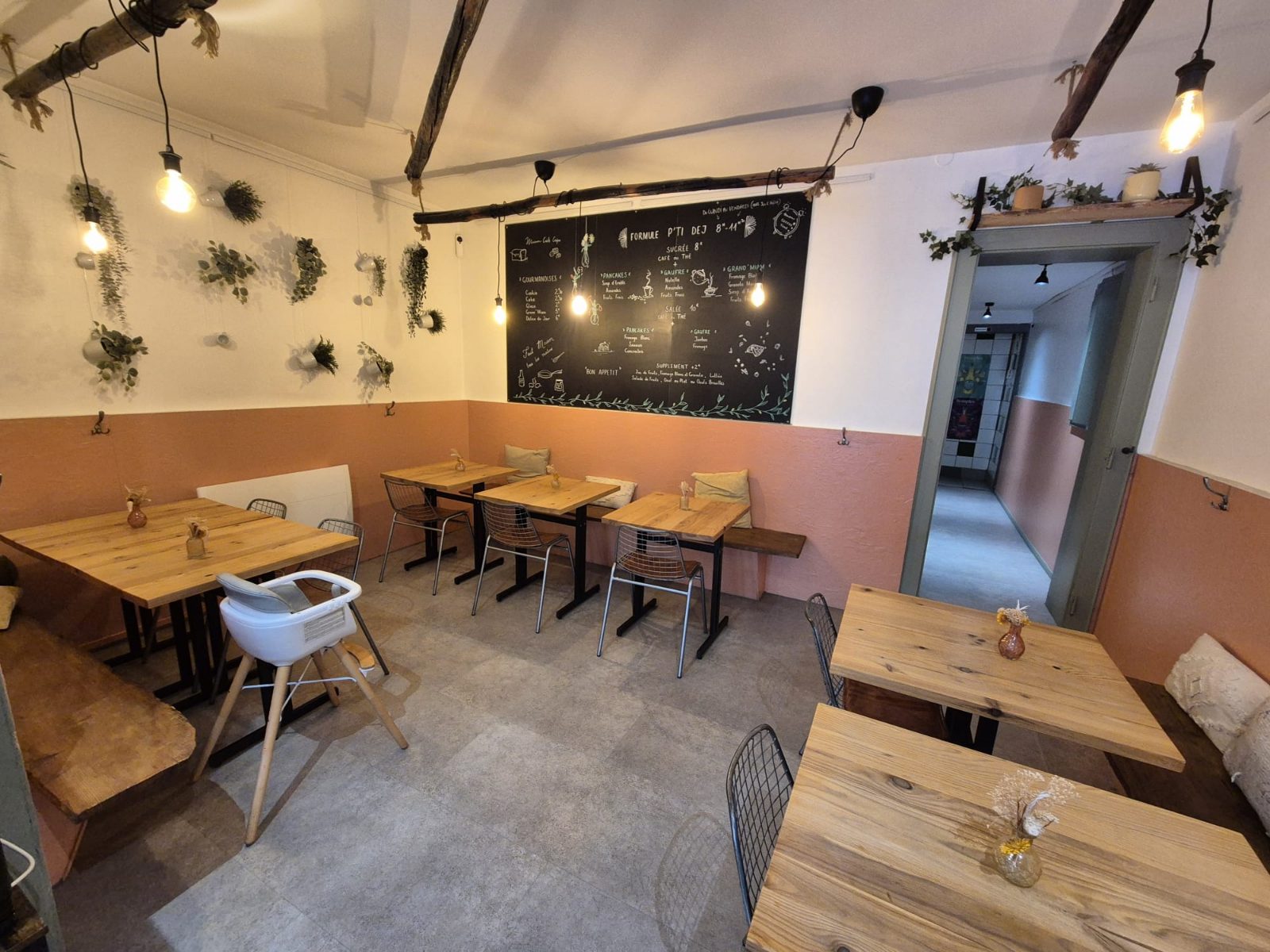 Salle avec une chaise haute installée à côté des tables, sous l'ardoise des formules du petit-déjeuner